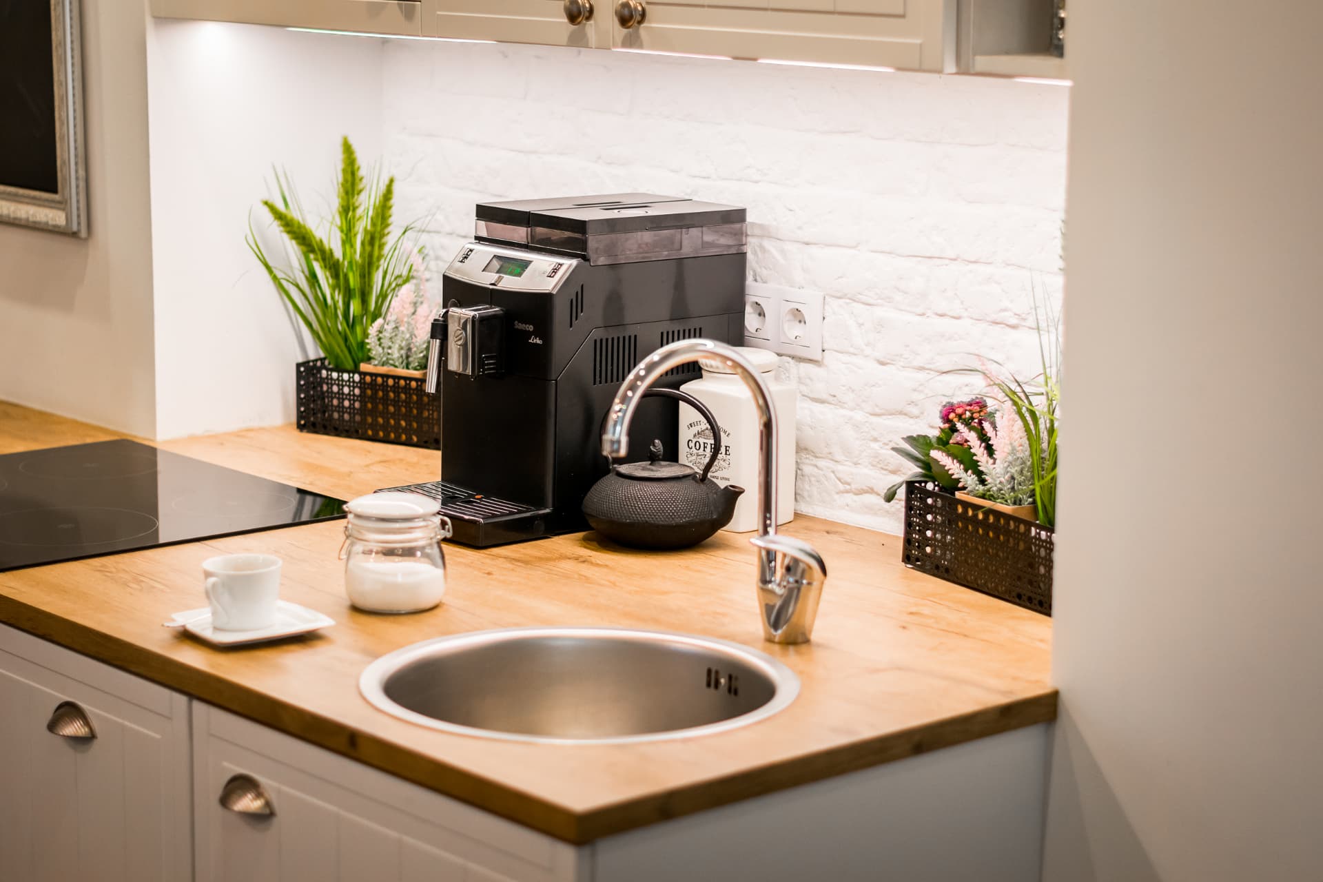 Kitchen detail with timber worktop, sink and coffee station against a white brick wall