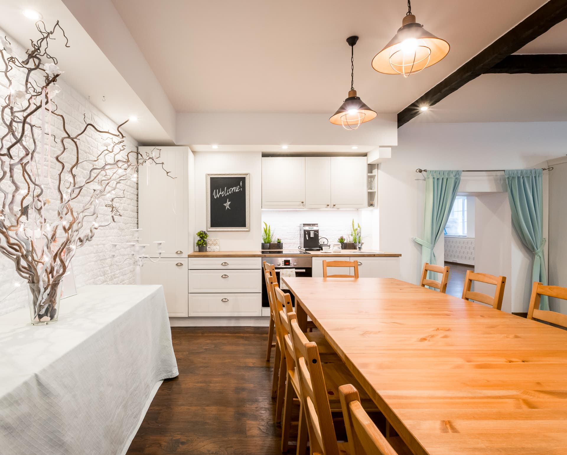 Event studio kitchen and gathering table beneath industrial pendant lights and dark ceiling beams