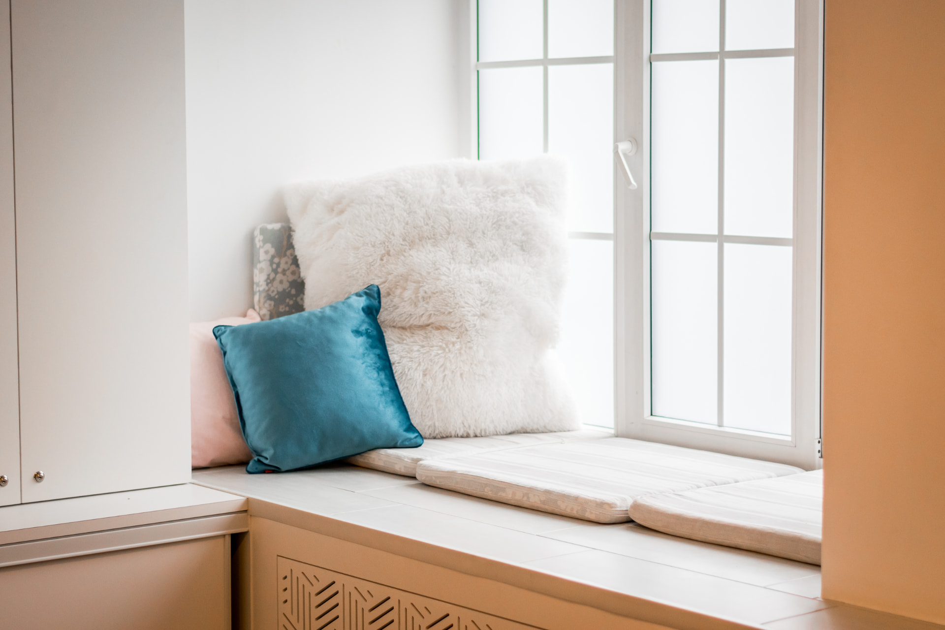Window seat with soft cushions above a custom geometric radiator cover