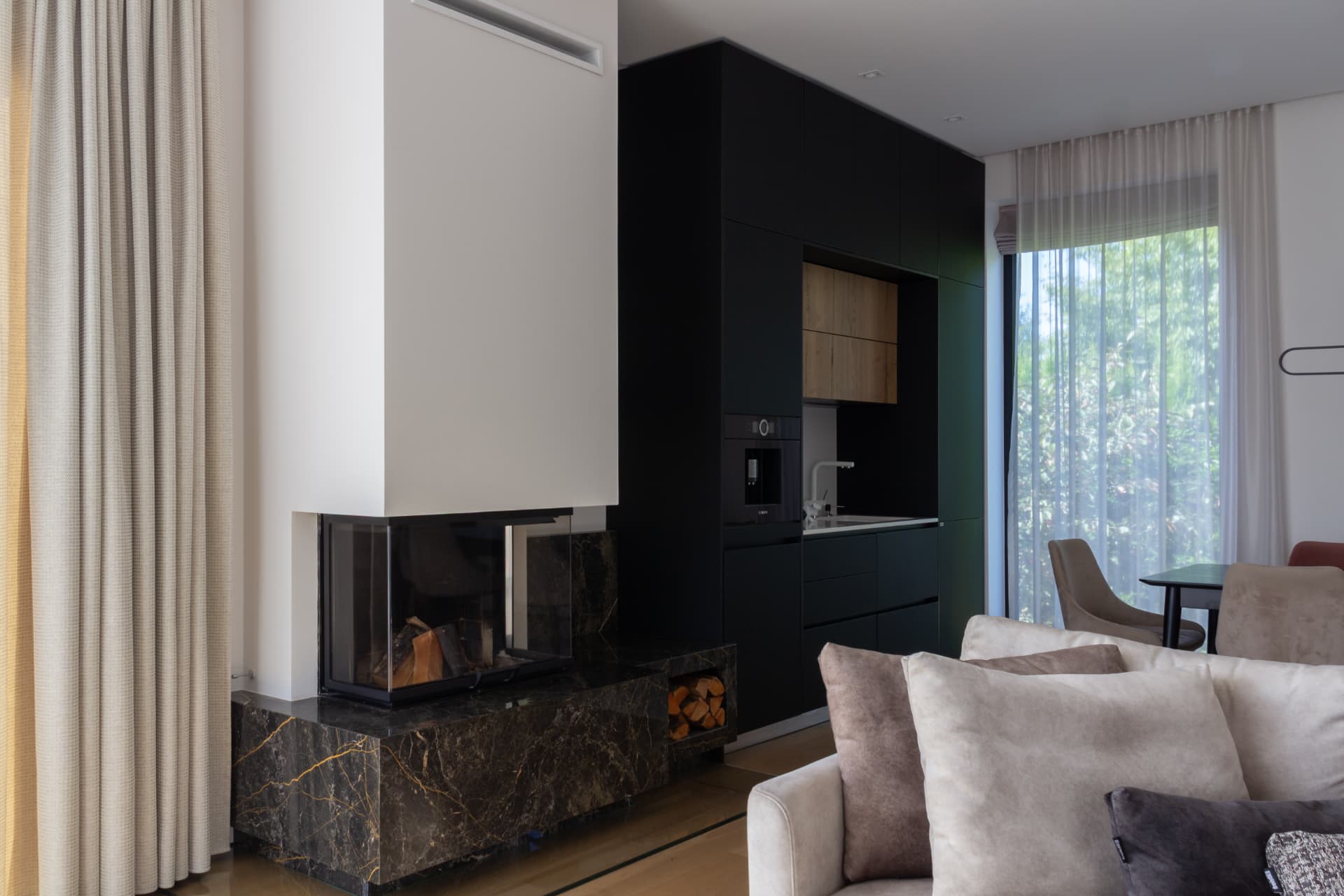 Living room from the side, showing the fireplace, black kitchen cabinetry and dining area