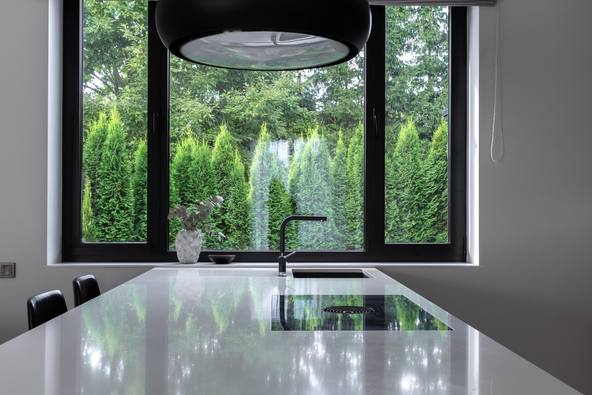 Kitchen island beneath a large black pendant, with black-framed windows onto the garden