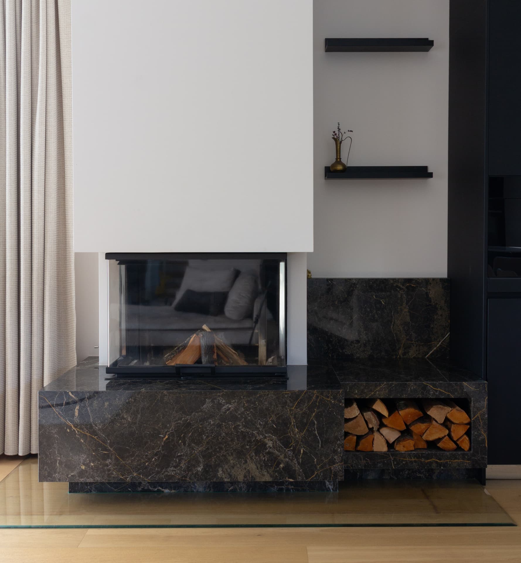 Black marble fireplace with an open firebox, shelves and stacked firewood