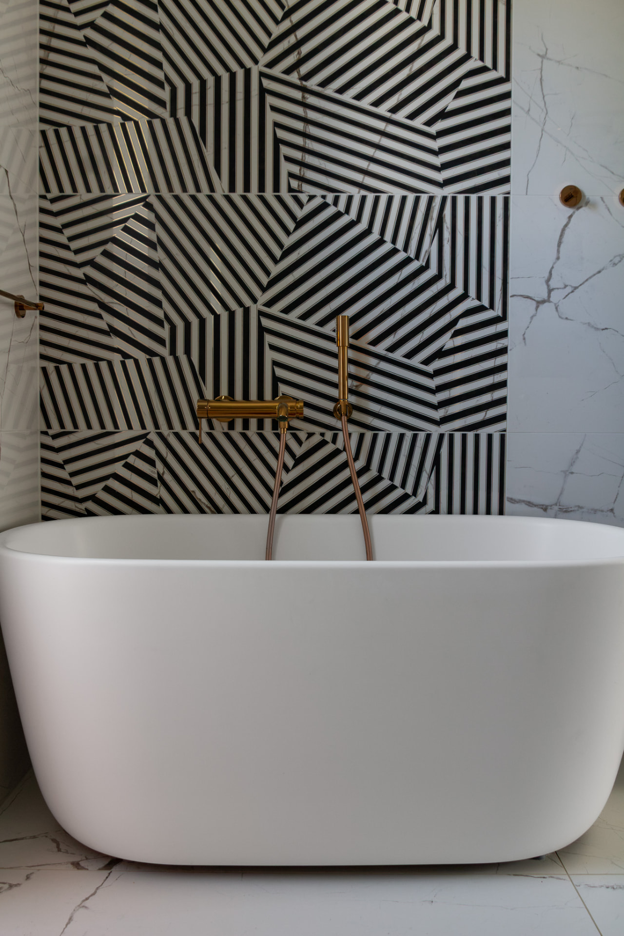White freestanding bathtub against a geometric black-and-white tiled wall