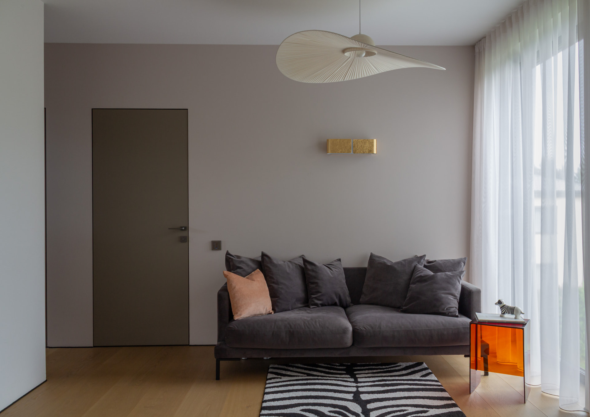 Grey sofa beside a transparent orange side table beneath a white sculptural pendant