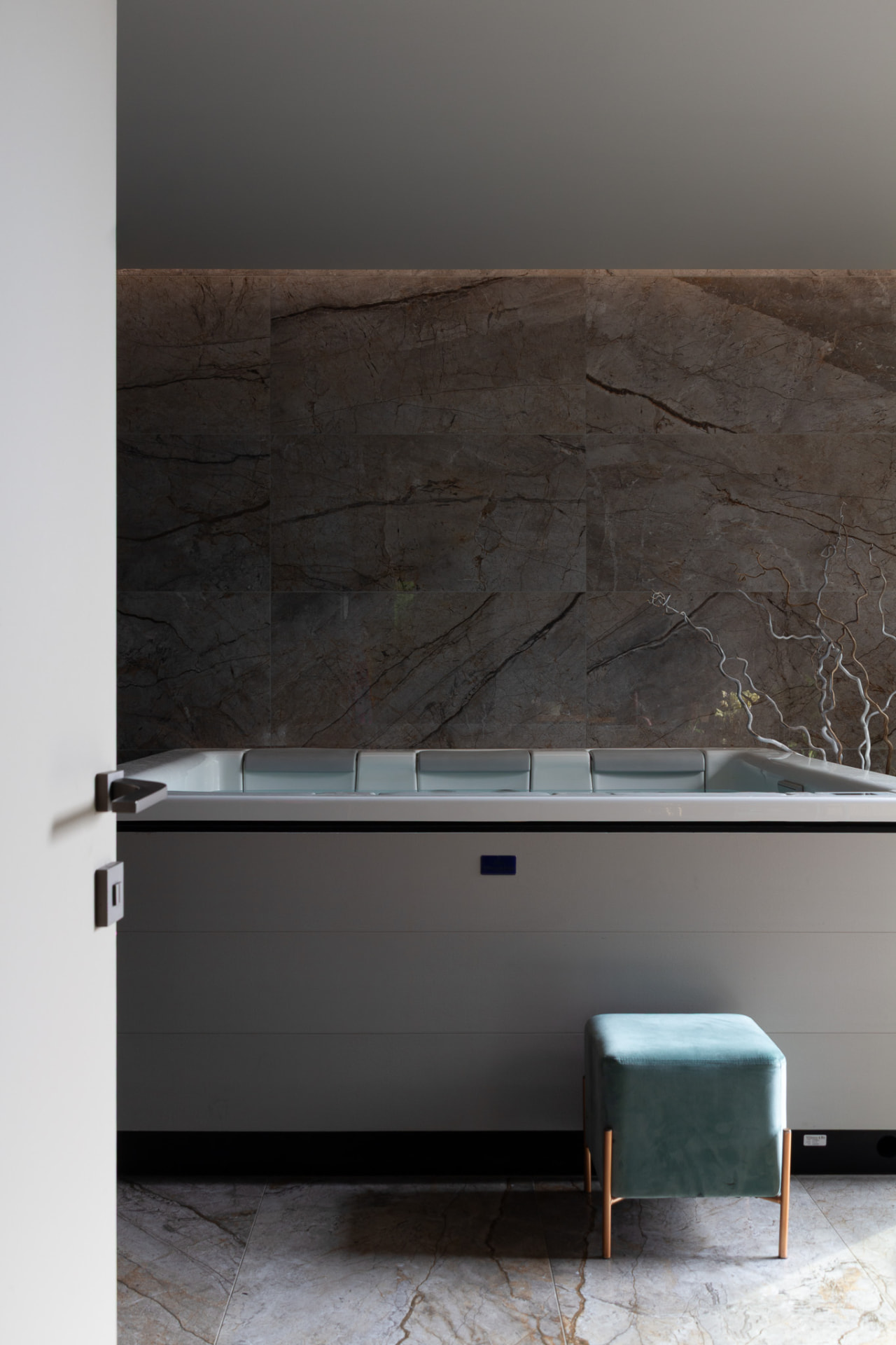 Main bathroom with dark natural stone, a built-in bath and a soft green stool